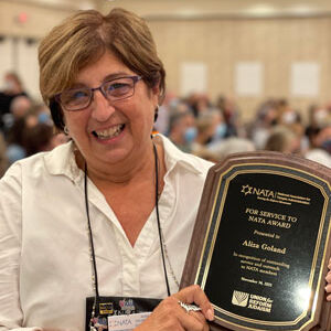 Aliza Goland holding up her award and smiling at camera with conference attendees in the background